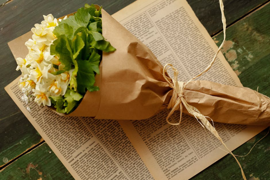 A floral arrangement featuring fresh white and yellow daffodils with long green stems, placed on a white surface alongside two halves of a lemon cut to reveal their juicy orange interior. The daffodil